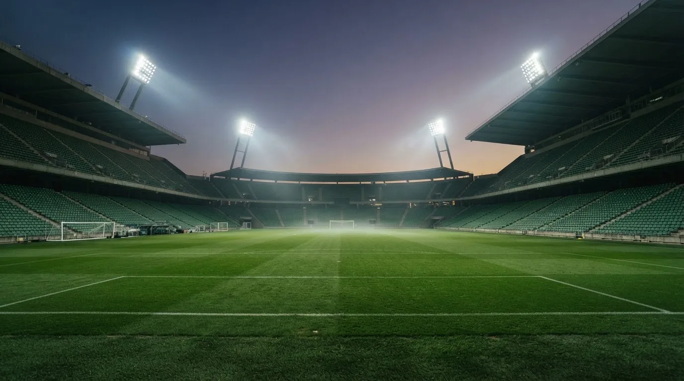 Een leeg voetbalstadion met lichtmasten bij schemering