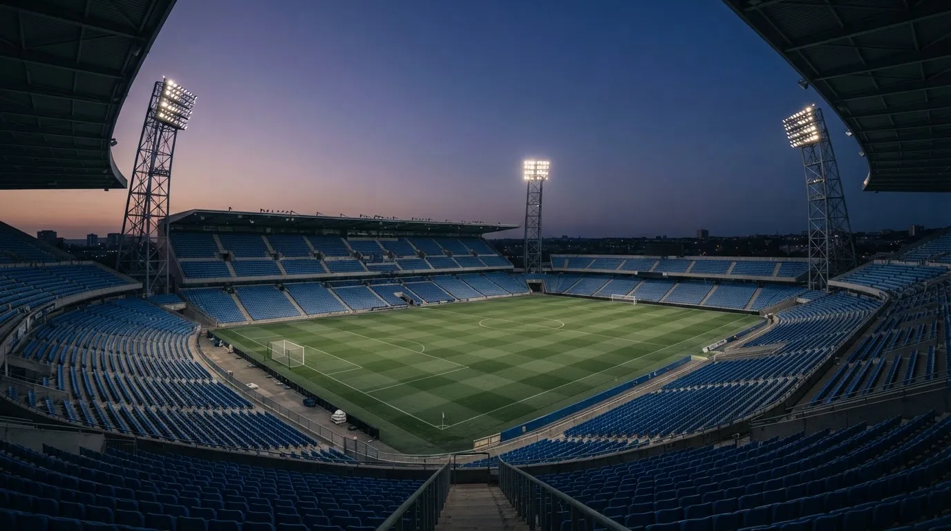 Een leeg voetbalstadion met lichtmasten bij schemering