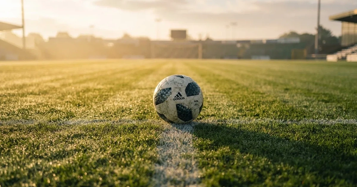 Een voetbal op de middenstip van een grasveld in het ochtendlicht