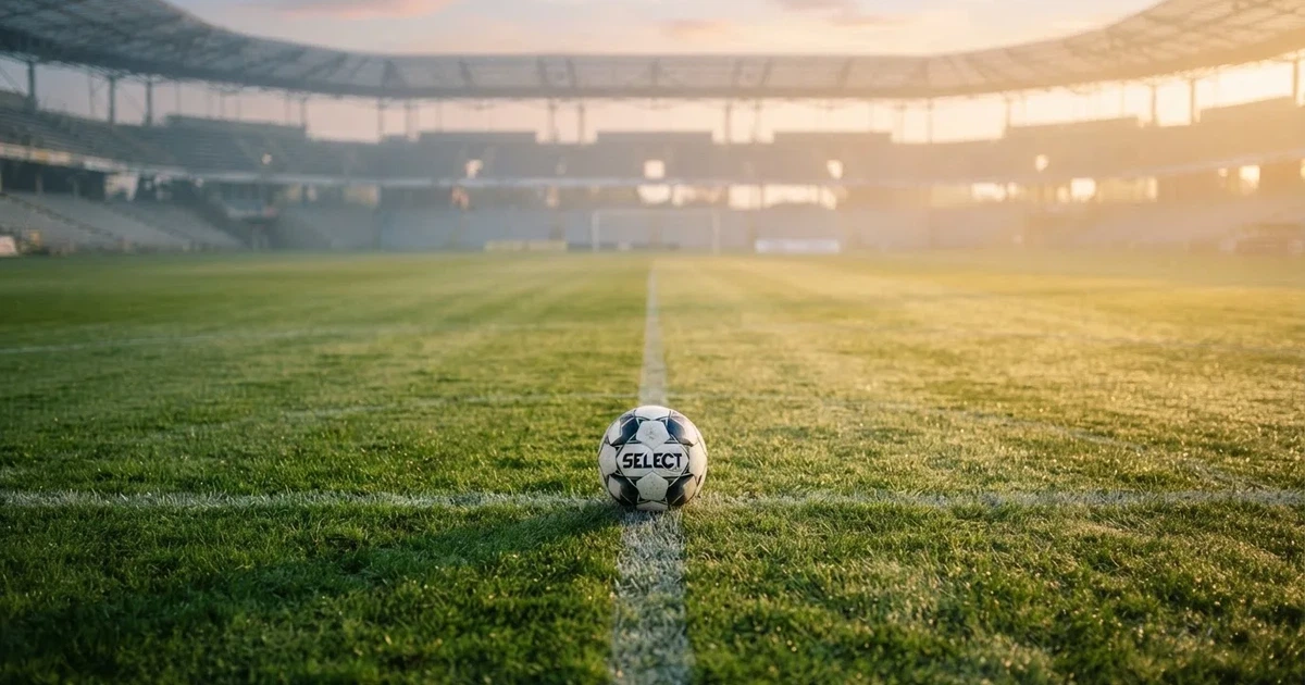 Een voetbal op de middenstip van een grasveld in het ochtendlicht