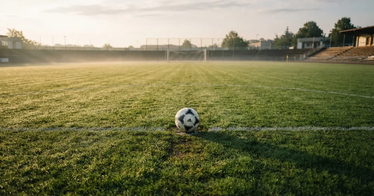 Een voetbal op de middenstip van een grasveld in het ochtendlicht