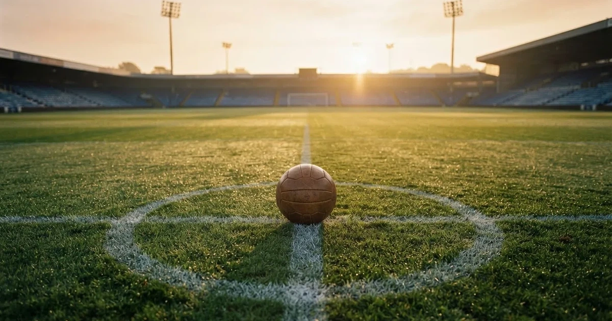 Een voetbal op de middenstip van een grasveld in het ochtendlicht