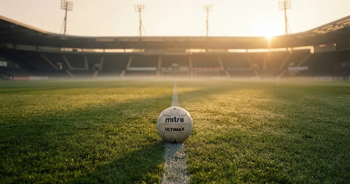 Een voetbal op de middenstip van een grasveld in het ochtendlicht