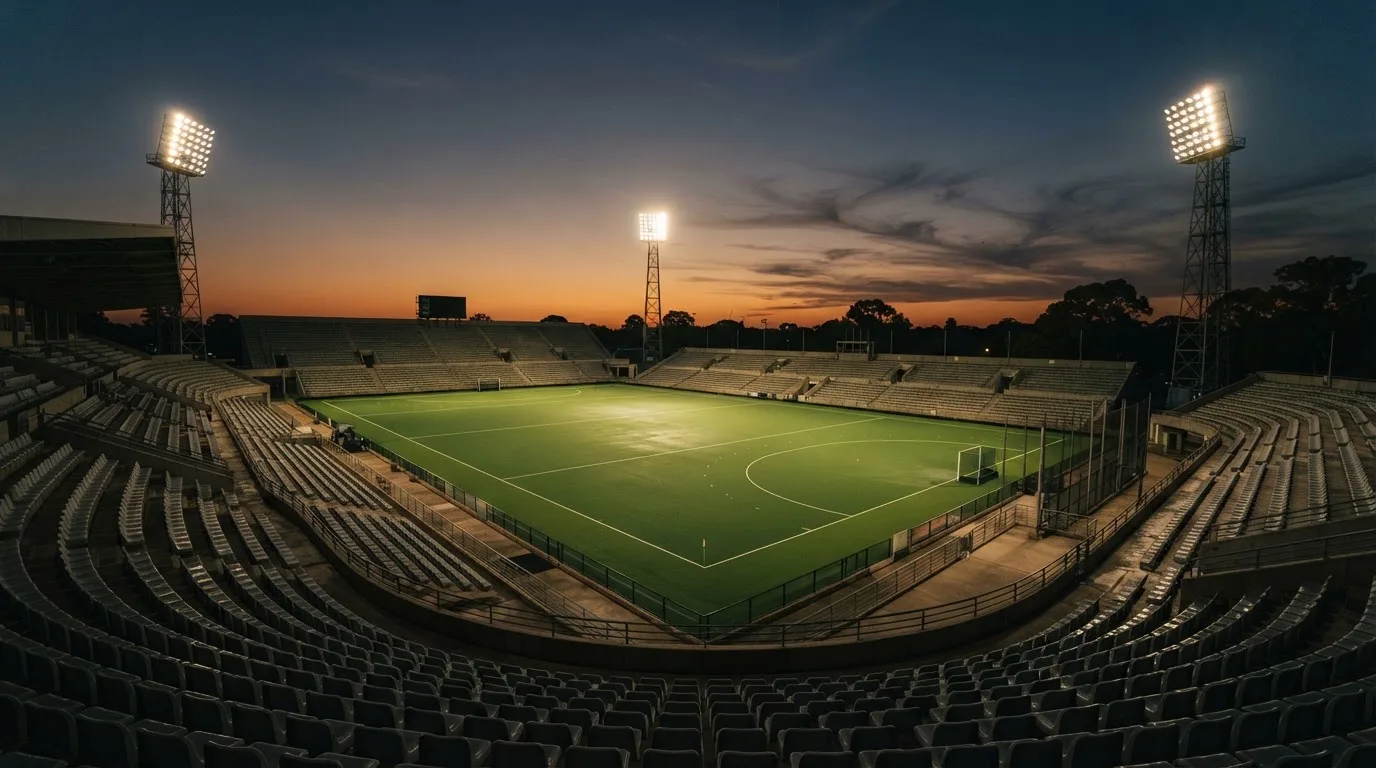 Een leeg voetbalstadion met lichtmasten bij schemering