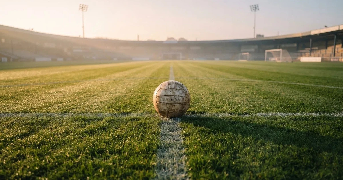 Een voetbal op de middenstip van een grasveld in het ochtendlicht