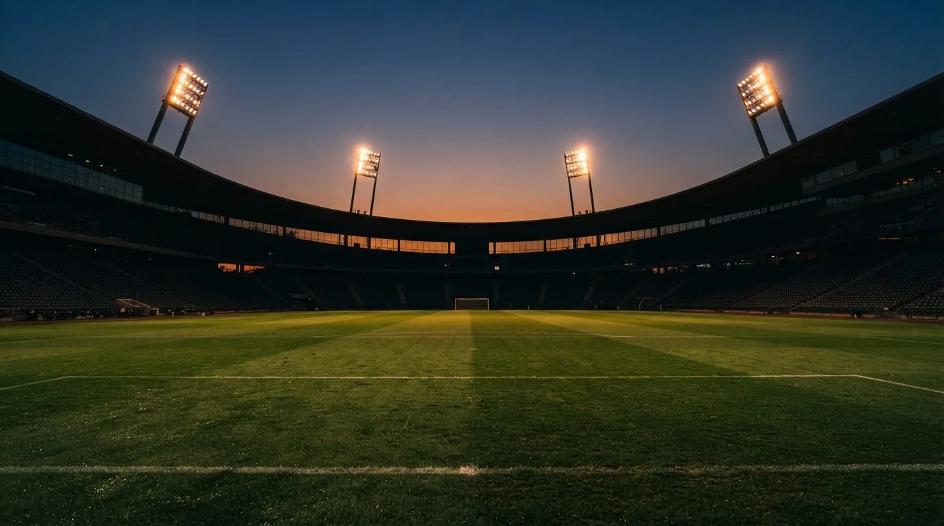 Een leeg voetbalstadion met lichtmasten bij schemering