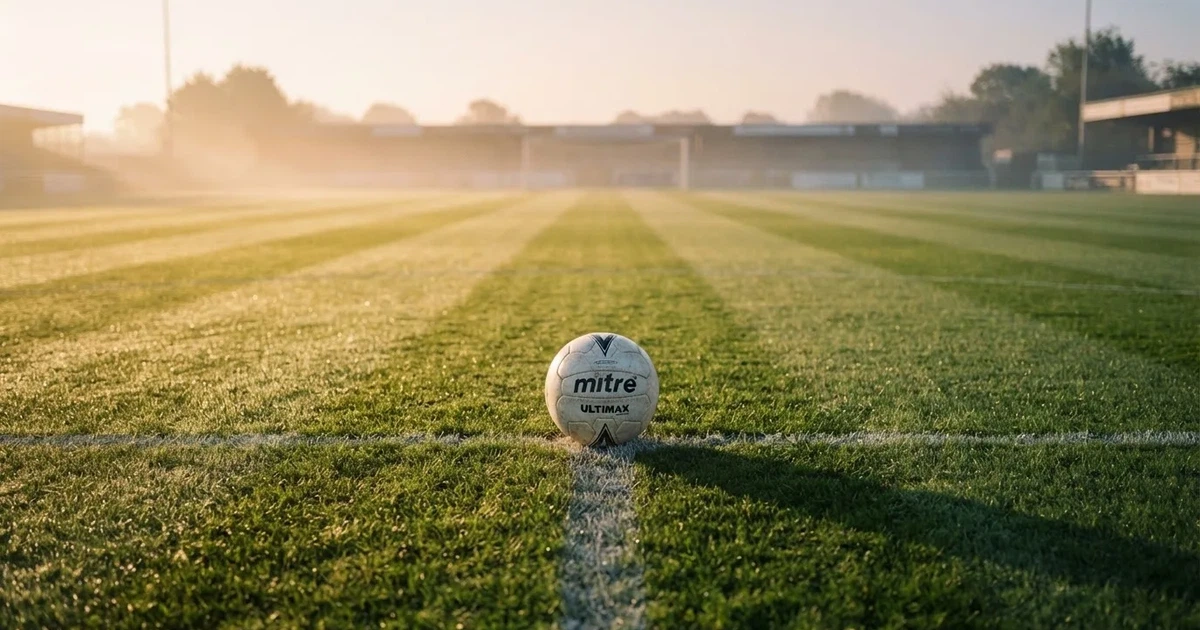 Een voetbal op de middenstip van een grasveld in het ochtendlicht