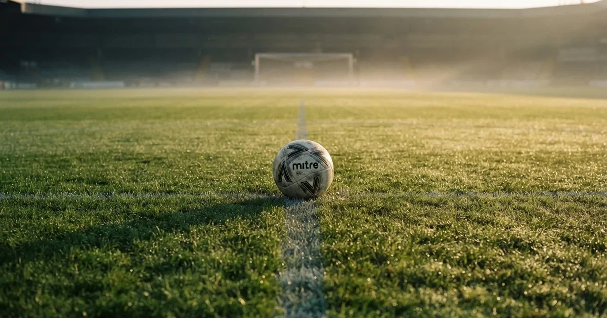 Een voetbal op de middenstip van een grasveld in het ochtendlicht
