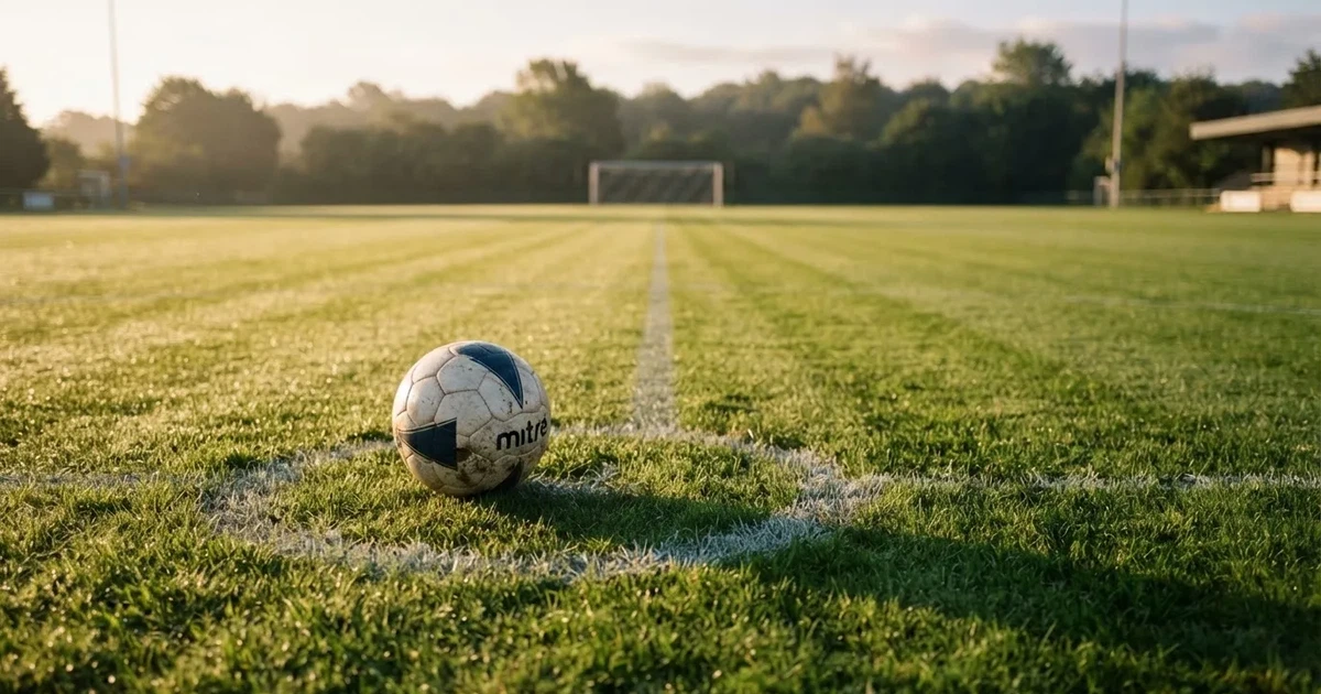 Een voetbal op de middenstip van een grasveld in het ochtendlicht