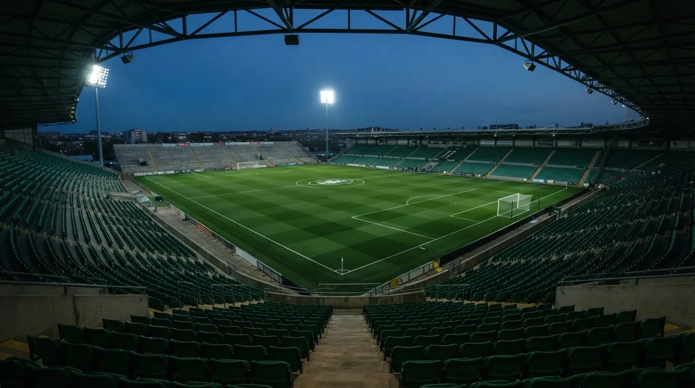 Een leeg voetbalstadion met lichtmasten bij schemering
