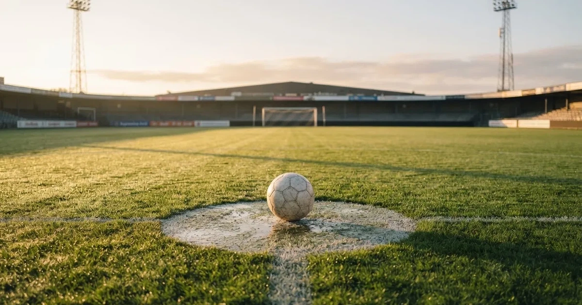 Een voetbal op de middenstip van een grasveld in het ochtendlicht